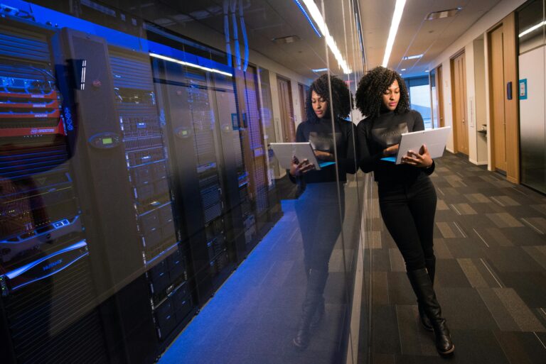 A woman using a laptop navigating a contemporary data center with mirrored servers.