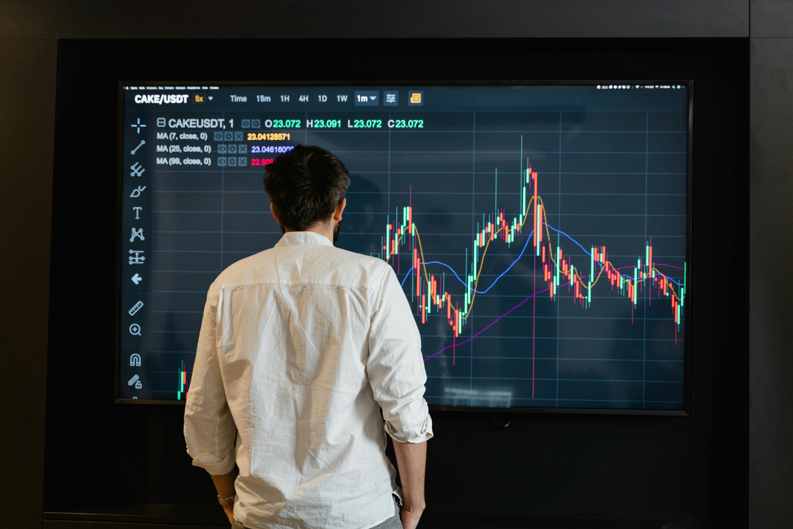 Back view of a trader analyzing cryptocurrency data on a monitor indoors.