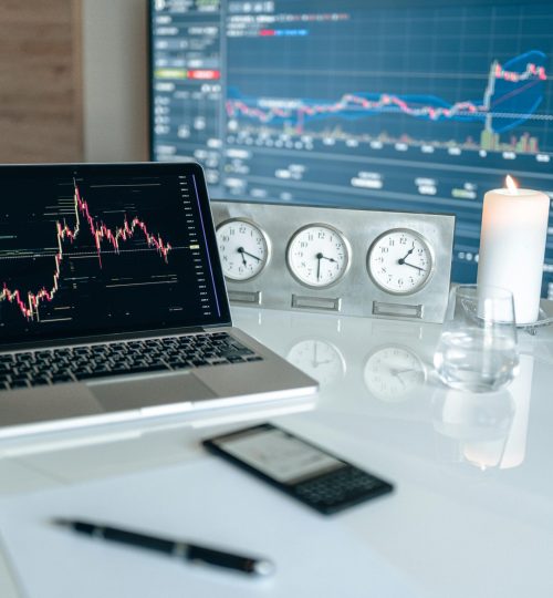 A modern workspace featuring financial charts and multiple clocks on a white table, ideal for trading.